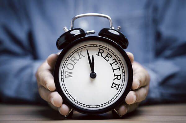 Person holding alarm clock with hands pointing in between the words "Work" and "Retire".