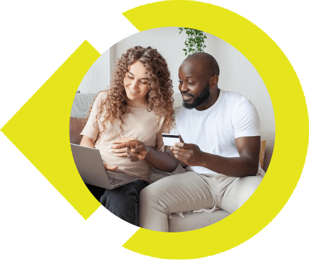 Multi-racial couple sitting on couch using credit card and looking at laptop screen.