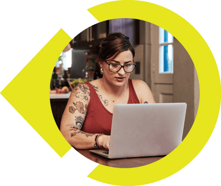 Young woman with tattoos and glasses sitting at table working on laptop.