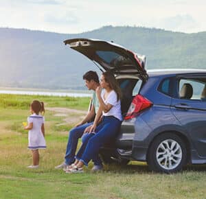 Family of three enjoying view from the trunk of small car.