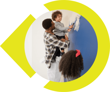Father holding son up to wall to paint while daughter looks up from below.