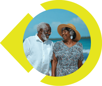 Older couple smiling at one another while walking on beach.