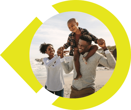 Family of three holding hands of child on father's neck while walking on the beach.